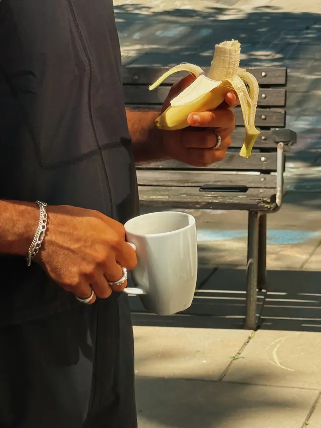 A hand holding a banana and a coffee